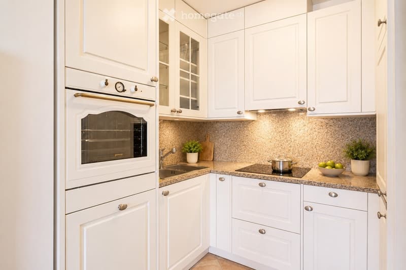 Modern kitchen with white cabinets, granite countertops, built-in oven, sink, and small decorative items.