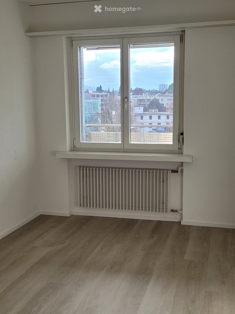Unfurnished Room. Empty room with wooden flooring, white walls, large window with radiator below, and a view of the cityscape.