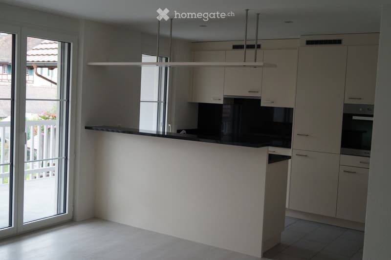 Modern kitchen with white cabinets, black countertop, and built-in oven. Features a large window and sliding glass door leading to a balcony.
