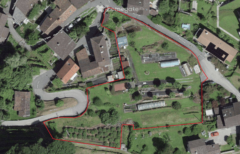 Aerial view of a residential area with multiple buildings, roads, and green spaces. The highlighted area is outlined in red, showing a specific property or lot.