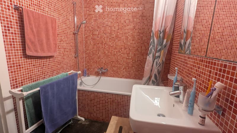 Bathroom with red tiled walls, a bathtub, a sink, a towel rack with towels, and a toothbrush holder on the sink counter.