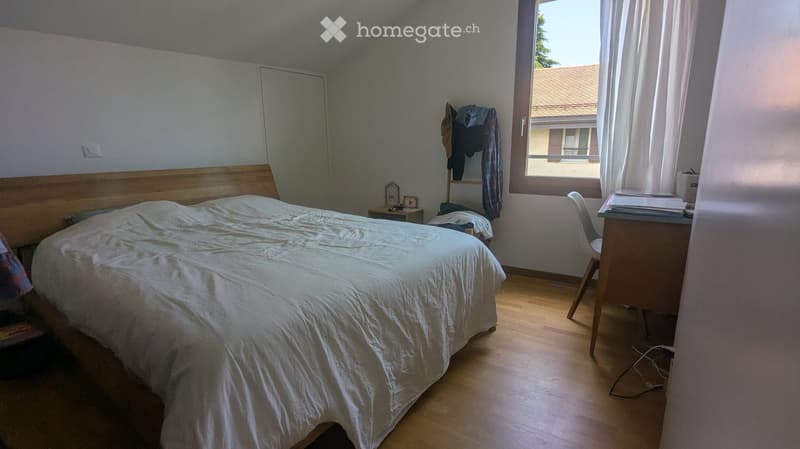 Bedroom with a wooden bed, nightstand, desk, chair, and wardrobe. Light-colored bedding and wooden flooring.