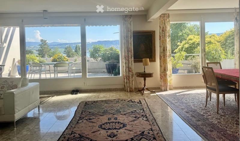 Bright living and dining area with large windows offering a scenic view, furnished with a sofa, dining table, chairs, side table, and lamps.