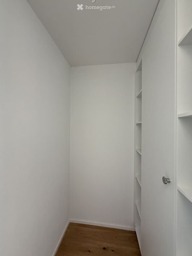 Empty room with white walls, wooden floor, and built-in shelving unit on one wall.