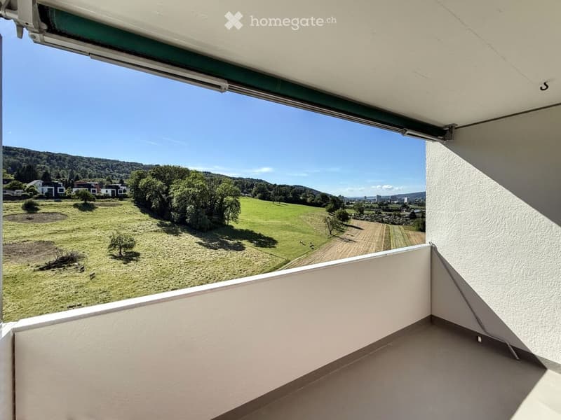 Balcony with expansive view of green fields, trees, and distant houses under a clear blue sky.