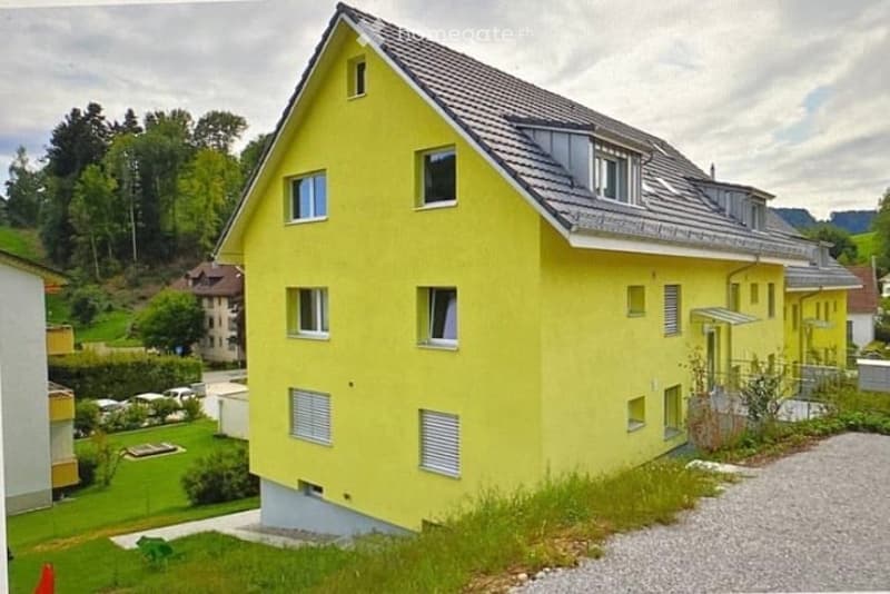 Bright yellow two-story house with gray roof and multiple windows, surrounded by greenery and a small garden area.