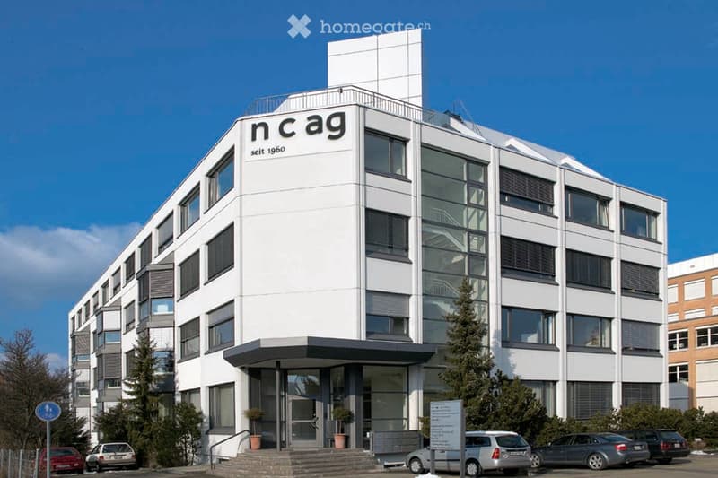 Modern multi-story building with white facade, large windows, and signage reading "ncag seit 1960".