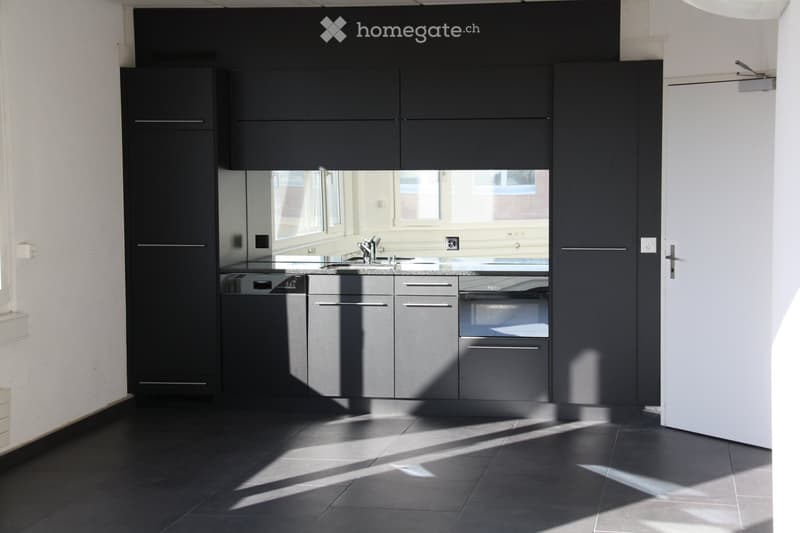 Modern kitchen with dark grey cabinets, stainless steel appliances, and a black tiled floor. Features a sink, faucet, dishwasher, and oven.