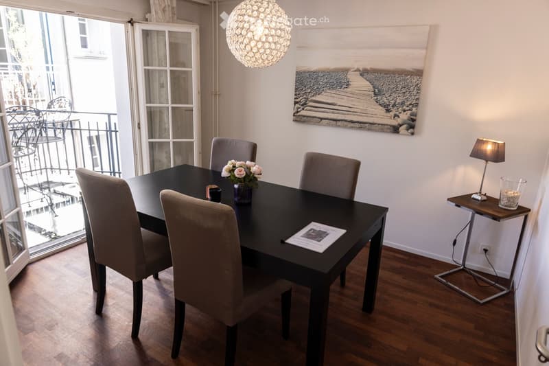 A dining room with a table, 4 chairs, lamp, artwork on the wall, and an open door leading to a balcony