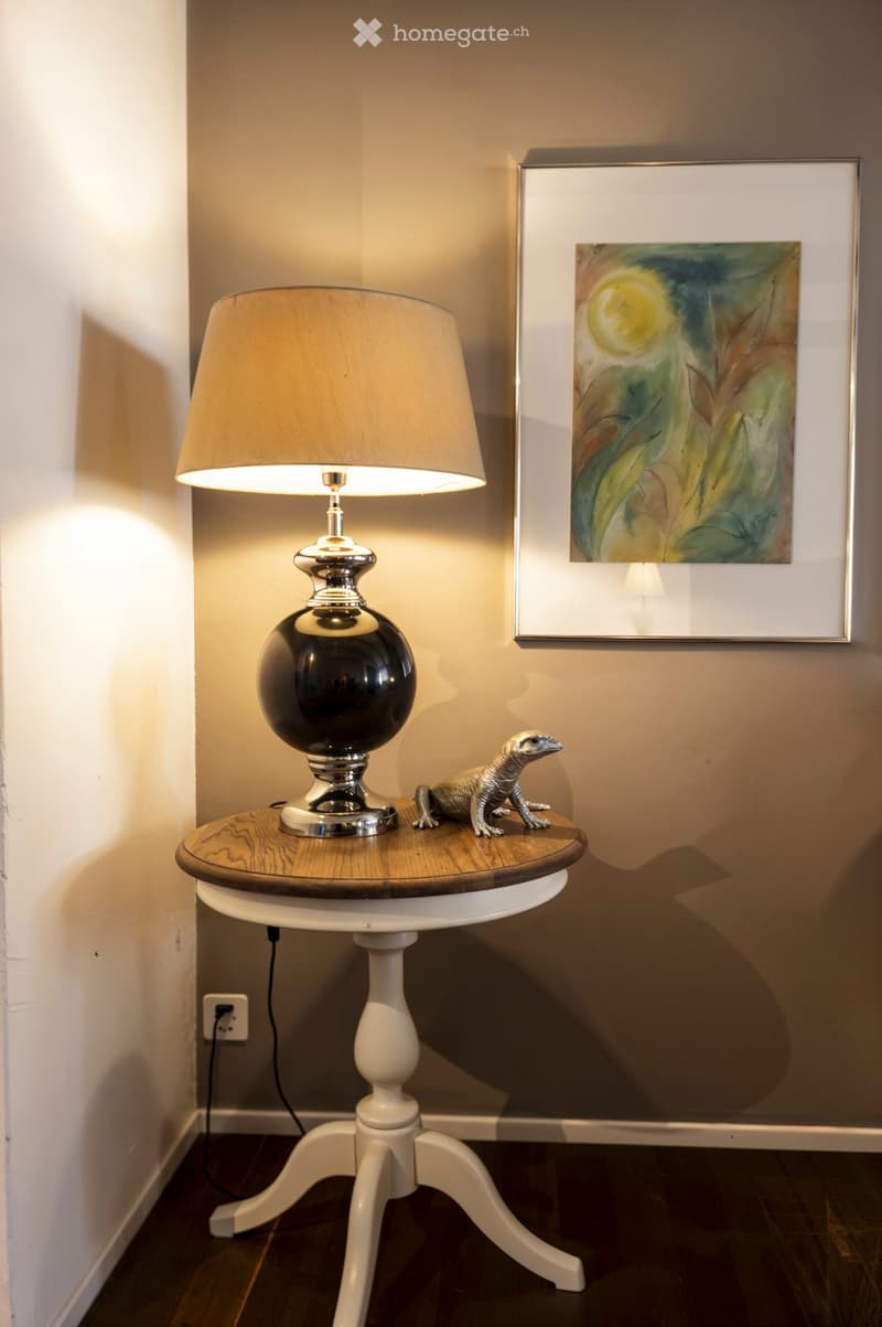room with a white table with a round wooden top, a black lamp with a white shade, a decorative lizard figurine, and a picture frame hanging on the wall