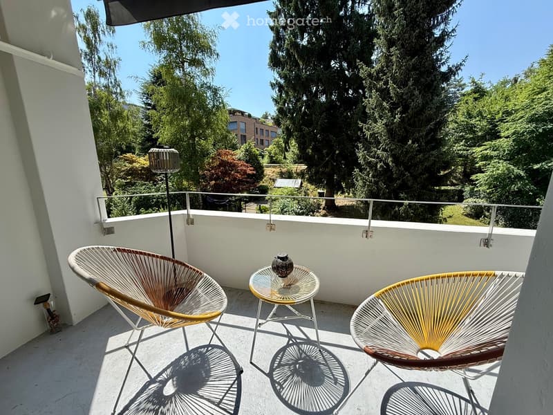 Balcony with two modern chairs, a small round glass table, and a decorative vase.