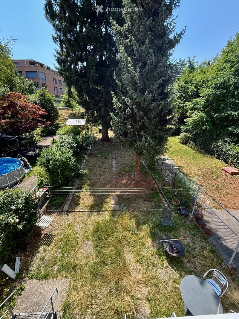 Garden with a grassy area, trees, a swimming pool, a barbecue, and outdoor furniture including a table and chairs.