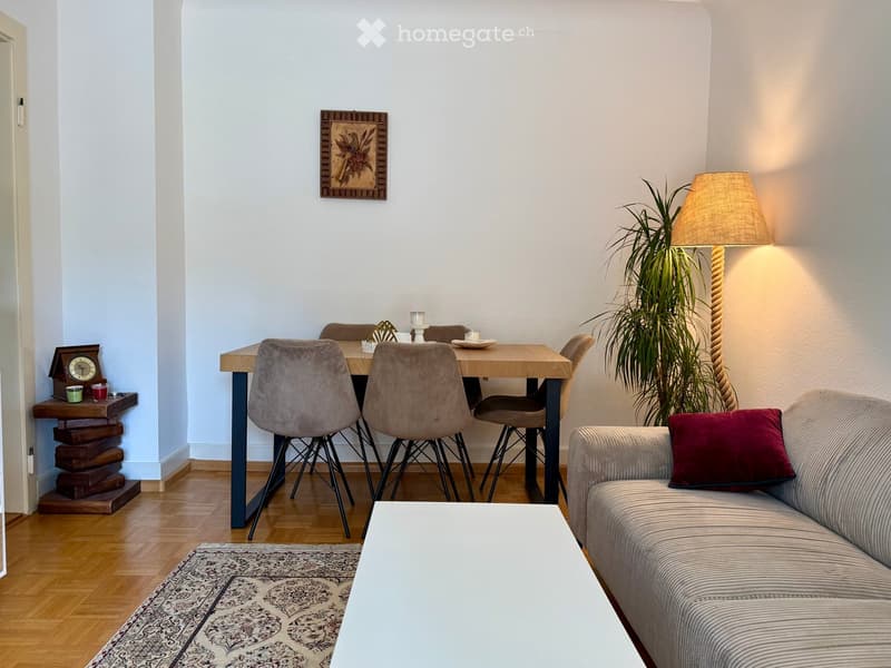 A modern living and dining area with a sofa, coffee table, dining table, chairs, a floor lamp, a plant, and a decorative clock on a side table.