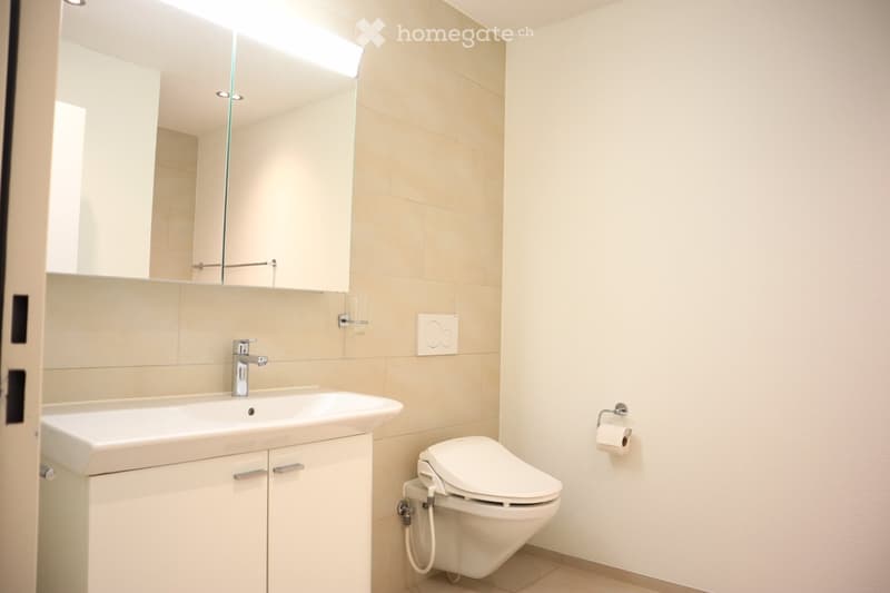 white bathroom with a sink, toilet, mirror, and wall-mounted toilet