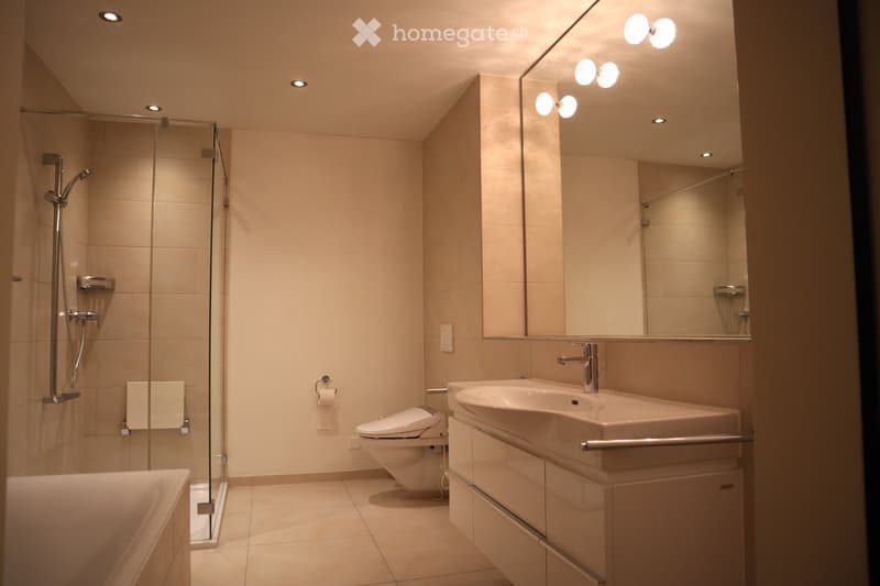 A bathroom with a bathtub, toilet, sink, and large mirror with spotlights
