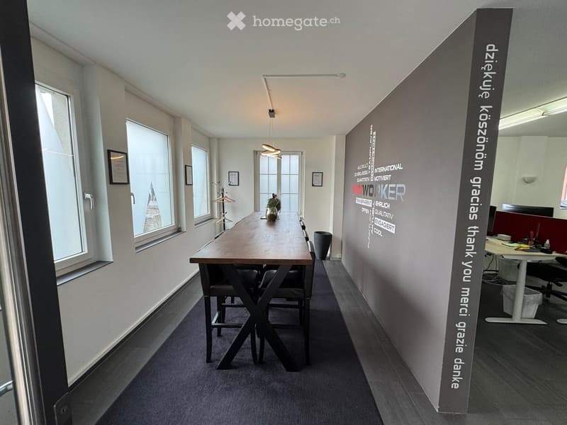 Dining room, large wooden table, chairs, carpet, wall with hanging clothes, windows, wall with writings