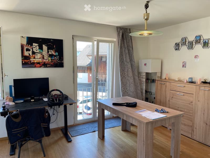 A room with a desk, chair, monitor, steering wheel, table, lamp, cabinet, shelf, rug, poster, picture frames, plate, doll, belt, and papers.