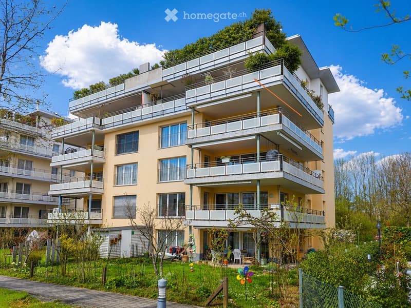 A multi-story residential building with balconies, large windows, and a well-maintained garden area in front.