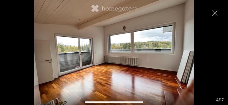 Empty room with wooden flooring, large windows offering a scenic view, and a sliding glass door leading to a balcony.