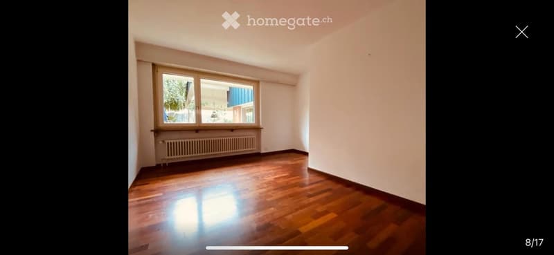 Empty room with wooden flooring, white walls, and a large window with a radiator below it.