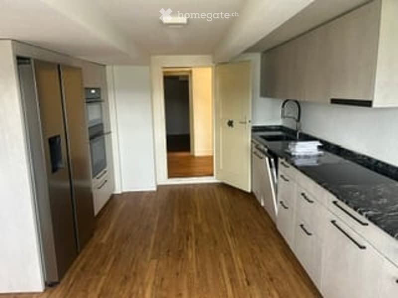 Modern kitchen with light-colored cabinets, black granite countertops, stainless steel appliances, and wooden flooring.
