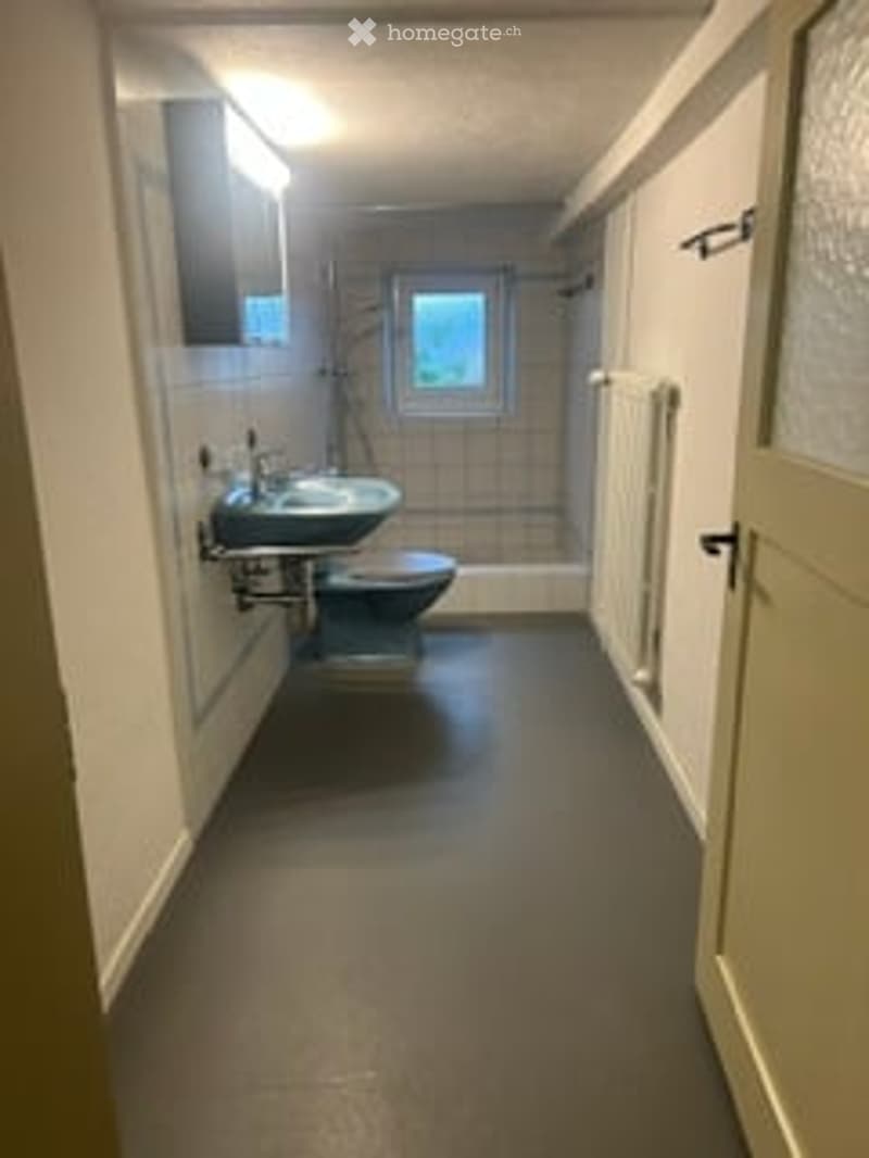 Small bathroom with a sink, toilet, mirror, and radiator. The floor is dark grey, and the walls are white with tiled sections.