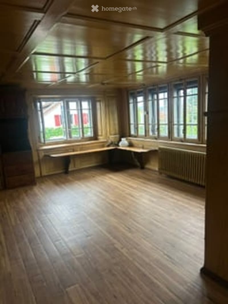 Empty room with wooden flooring, large windows, and a simple bench against the wall.