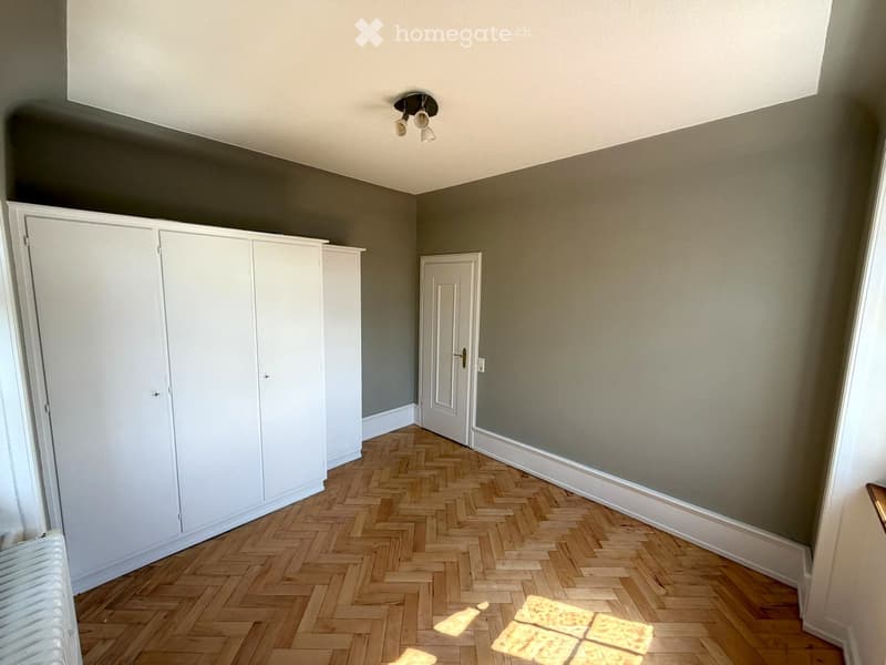 Empty room with wooden herringbone flooring, white built-in wardrobes, and a white door leading to another space.