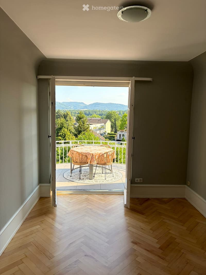 Open sliding doors lead to a balcony with a scenic view, featuring a small table and chairs.