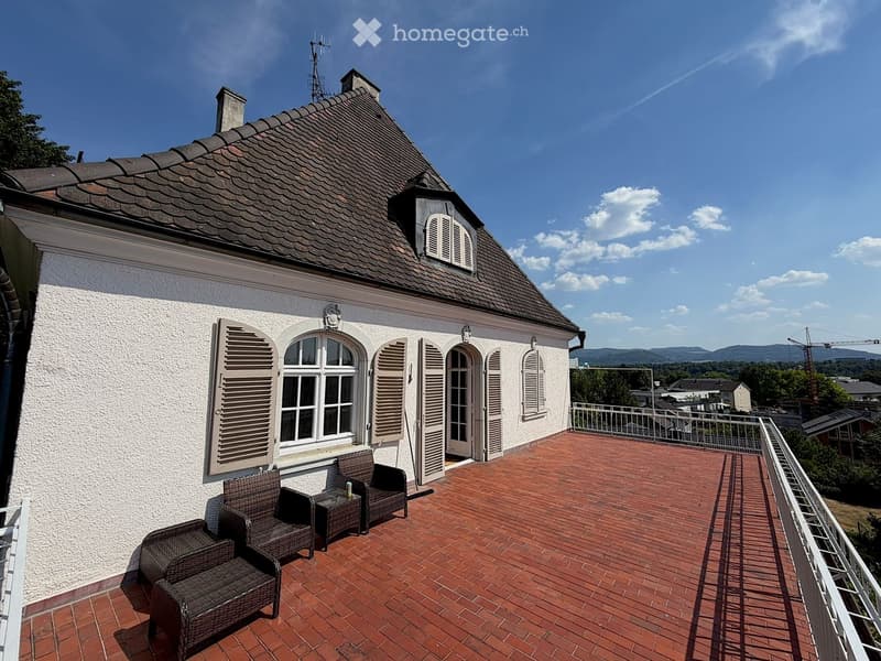 Balcony with brick tiles, metal railing, and several wicker chairs and a small table.