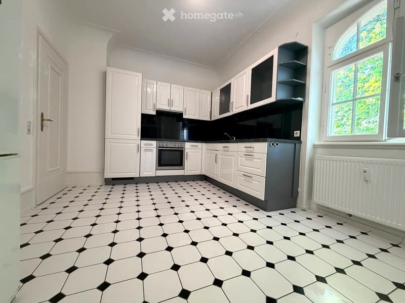 Modern kitchen with white cabinets, black countertop, stainless steel oven, and black and white hexagonal tiled floor.