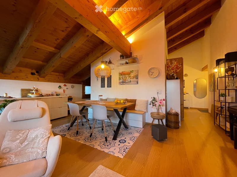 Cozy living and dining area with exposed wooden beams, a sofa, dining table with chairs, kitchen area, and decorative items.