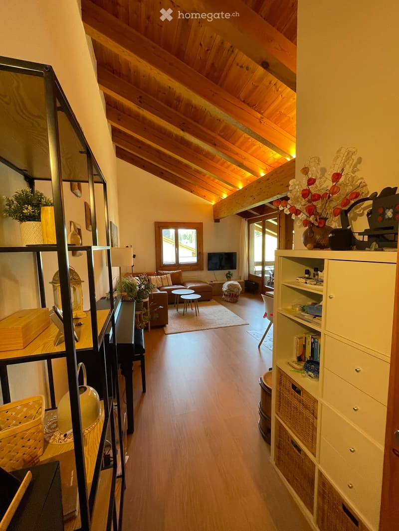 A cozy living room with wooden beams on the ceiling, a sofa, coffee table, stools, a bookshelf, and decorative vases.