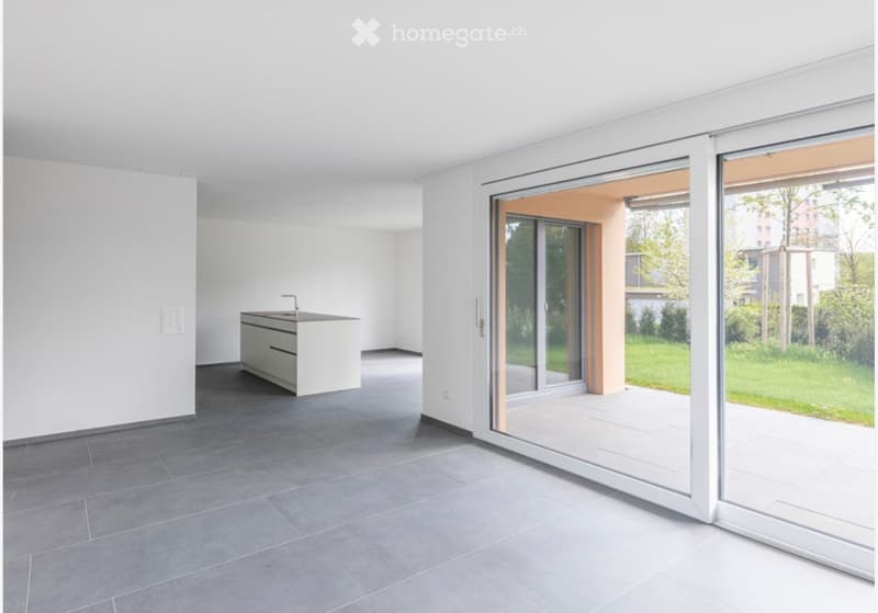 large room, white walls, tile floor, open door, kitchen, sliding glass door leading to a terrace with view of a green lawn