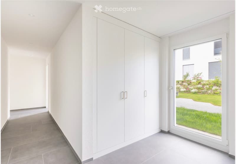 Empty room with a tiled floor, tall white cabinets, a sliding glass door, and a view of a garden.
