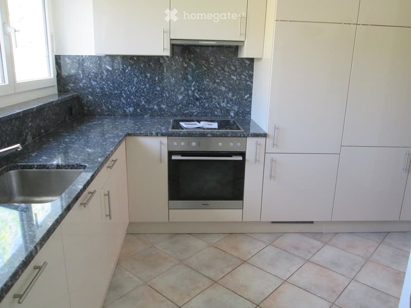 Modern kitchen with white cabinets, granite countertops, stainless steel sink, and oven. Features a tiled floor and a window on the left side.