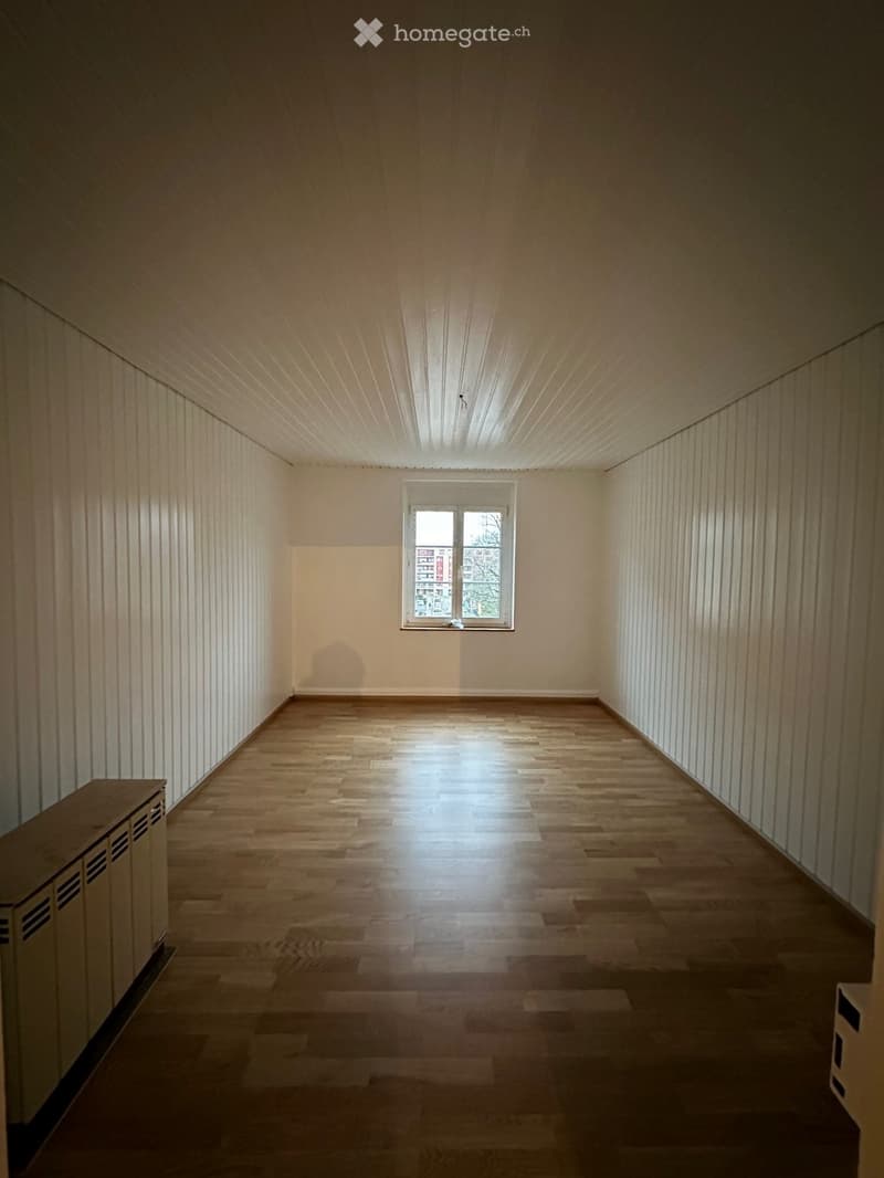Empty room with wooden flooring, white walls, and a single window letting in natural light.
