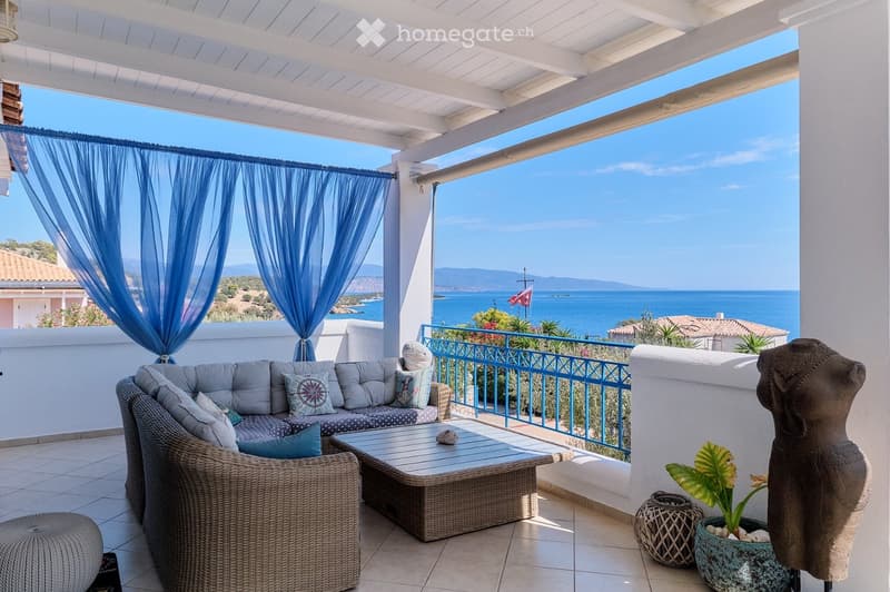 Balcony with a view of the sea, featuring a sofa, coffee table, wicker chair, plant, and decorative items.