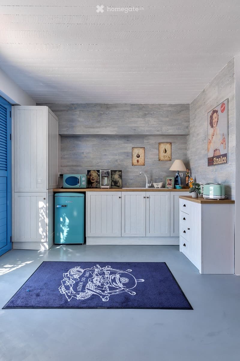 A modern kitchen with white cabinets, a turquoise refrigerator, a microwave, a toaster, a lamp, and a decorative rug on the floor.