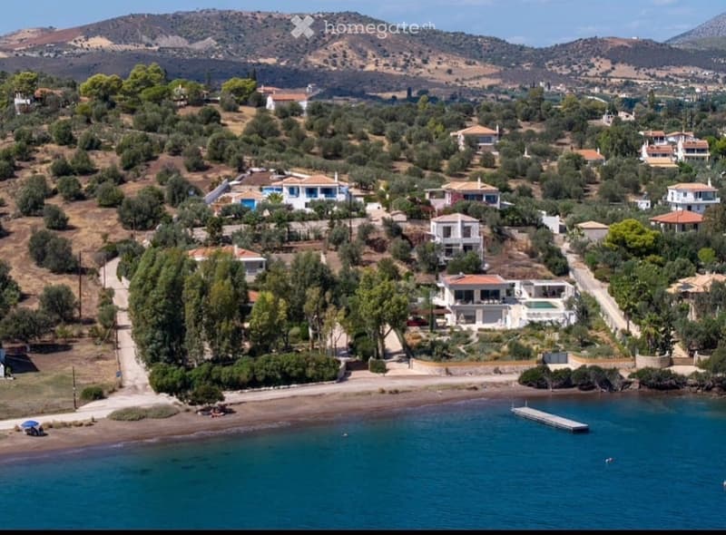 Aerial view of a coastal village with houses, trees, a swimming pool, and a beach.