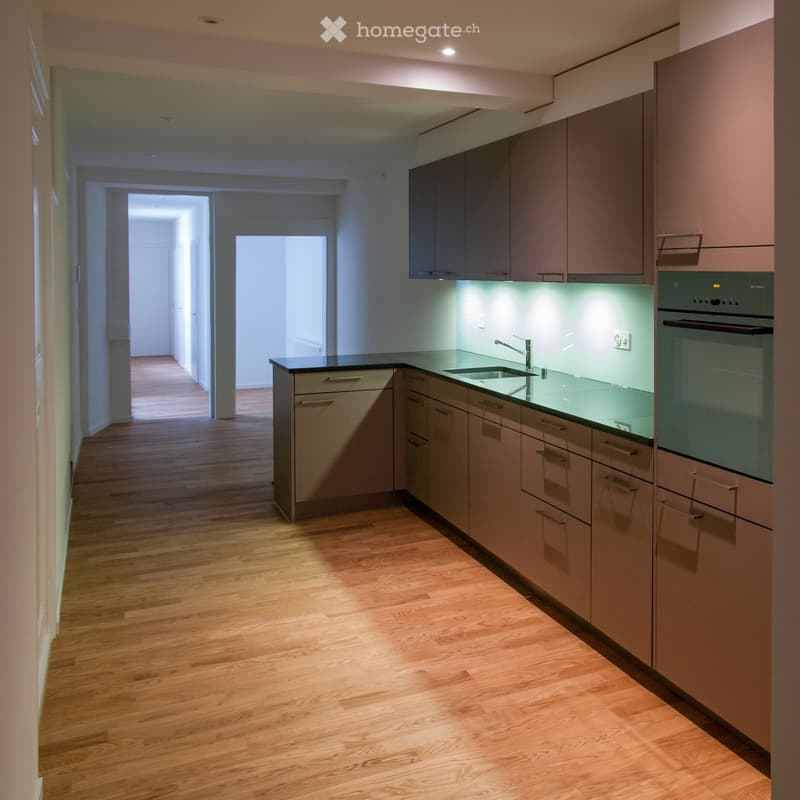 Modern kitchen with light wood flooring, sleek cabinetry, and built-in appliances including a sink, faucet, and oven.
