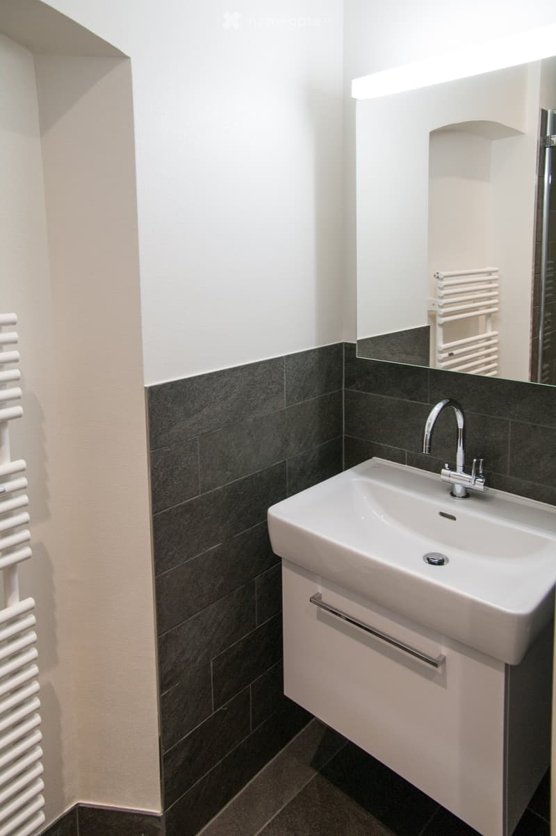 Modern bathroom with a white sink, chrome faucet, dark tiled walls, and a white radiator.
