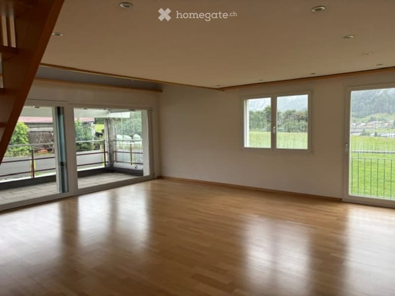 Empty room with wooden flooring, large windows, and sliding glass doors leading to a balcony.
