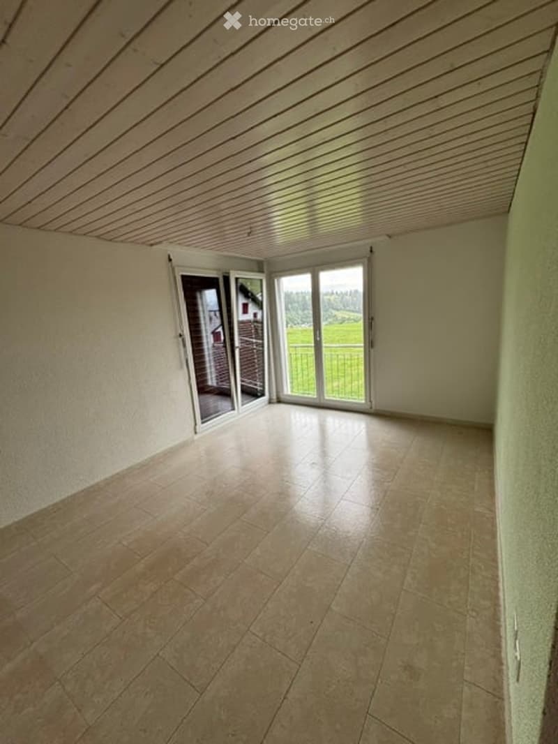 Empty room with tiled floor, white walls, and large sliding glass doors leading to a view of a green field.