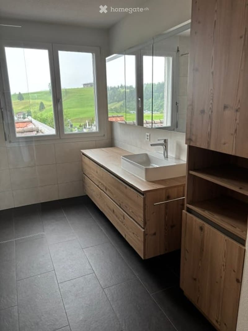 Modern bathroom with large windows offering a scenic view, featuring a wooden vanity with a sink and faucet, and built-in wooden cabinets.