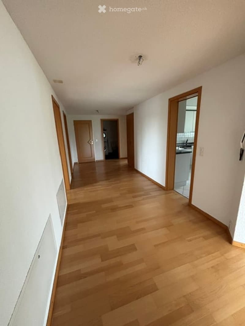 Empty hallway with wooden flooring, white walls, and several doors leading to different rooms.
