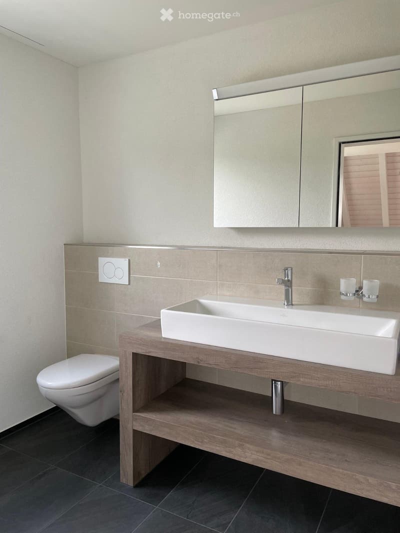 Modern bathroom with a white sink, wooden vanity, beige tiles, and a large mirror with built-in cabinets.