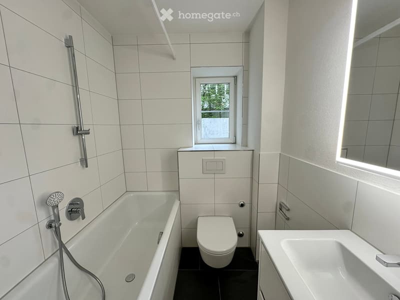 Modern bathroom with white tiles, bathtub, toilet, sink, and showerhead.
