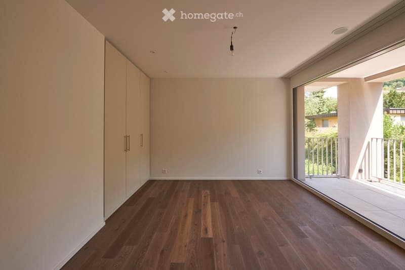 Empty room with wooden flooring, white walls, built-in closet, and large sliding glass door leading to a balcony.