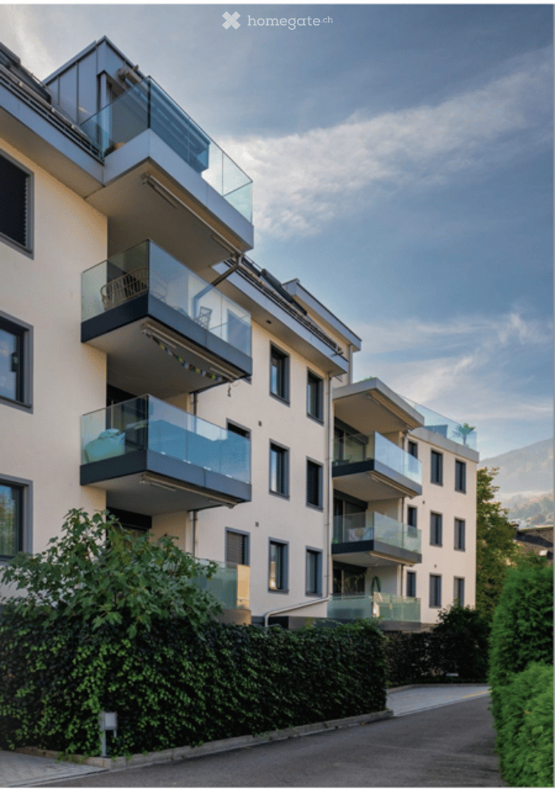 Modern multi-story apartment building with multiple balconies and a scenic mountain view in the background.